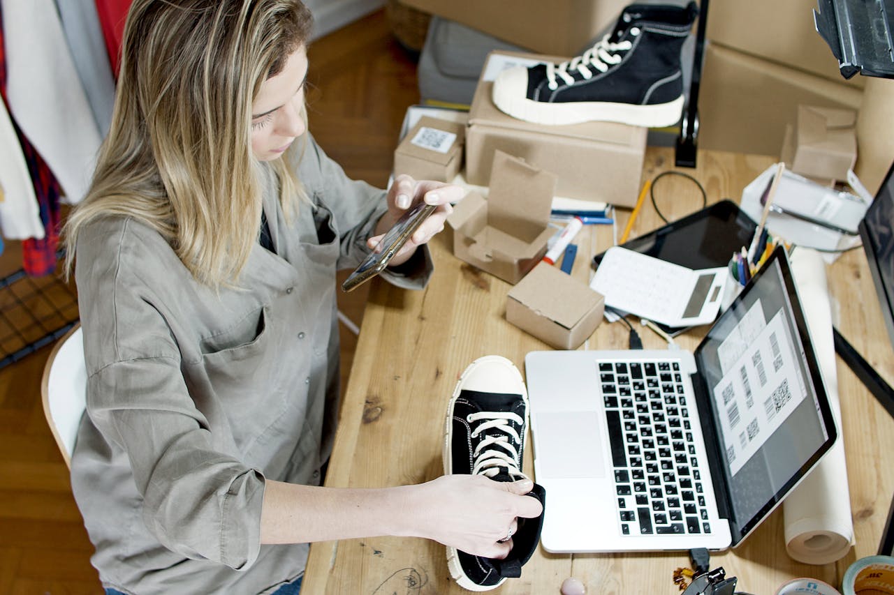 Home Woman photographing shoes for online sale in home workspace with laptop and packages.