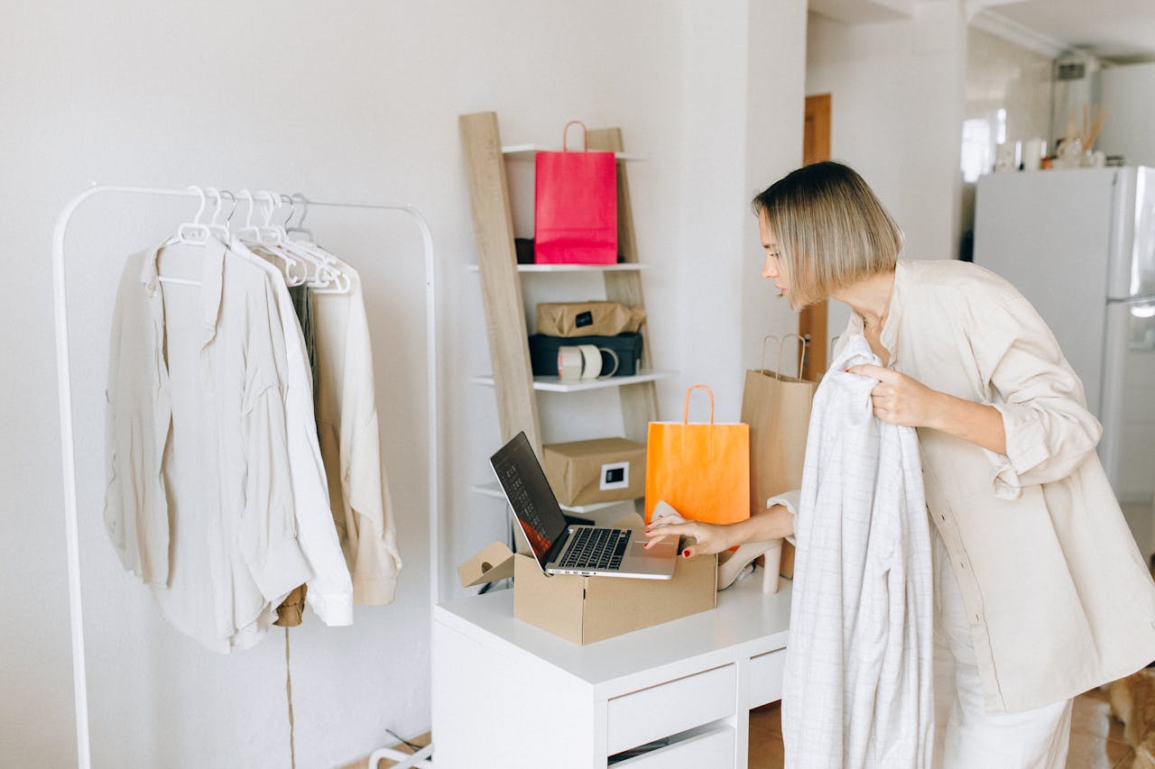 About A woman in casual attire unpacking a delivery box with clothing at home, engaging in online shopping.